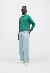 Polo vert à manches longues avec col, associé à un jean bleu clair oversize et des chaussures blanches. Design simple, matière en coton.