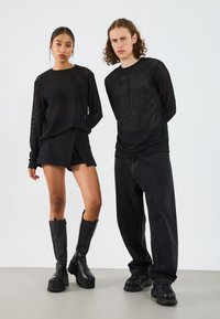 Black lightweight, textured long-sleeve tops paired with a black mini skirt and black knee-high boots. Male model in loose black jeans and sneakers.