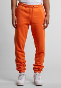 Orange Sweatpants aus weichem Material. Mit elastischem Bund und Kordelzug sowie Bündchen. Kleines Logo in der Nähe der Tasche.