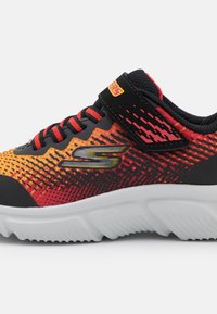 Baskets de sport noires et orange avec un motif texturé, dotées de lacets et d'une bande Velcro, et d'une semelle blanche rembourrée.