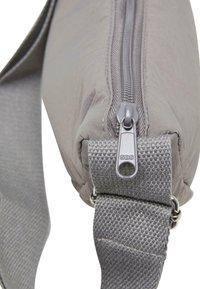 Gray fabric bag with a smooth texture, sturdy zipper, and adjustable woven strap featuring small metal hardware accents.