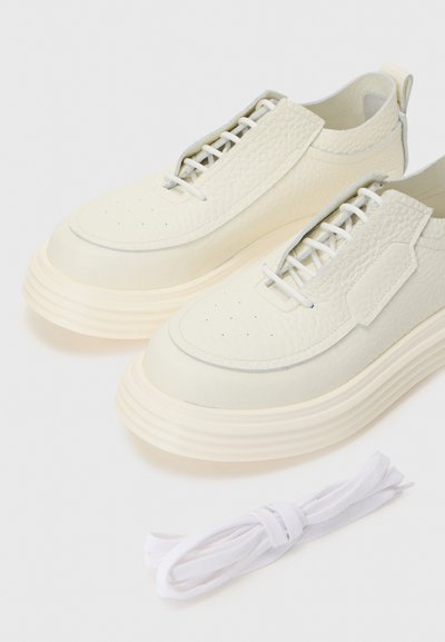 Lys beige lædersneakers med tekstureret overdel, rund tå og lagdelt hvid sål. Inkluderer ekstra flade hvide snørebånd.