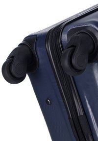 Valigia rigida blu navy con superficie testurizzata, doppie ruote nere e una robusta cerniera lungo il bordo.