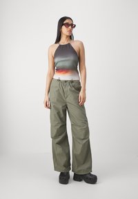 Top de halter com gradiente de cinza a laranja, combinado com calças cargo largas em verde-oliva e tamancos pretos de plataforma. Óculos de sol em forma de gato.