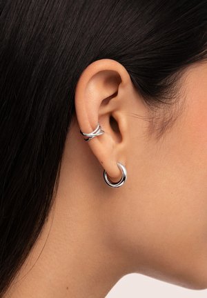 Silver hoop earrings, featuring a smooth, glossy finish with intertwined design elements and varying thickness. Worn on the outer ear.