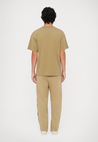 Korte mouwen, beige T-shirt met een relaxte pasvorm, gecombineerd met bijpassende beige sweatpants met een bedrukt ontwerp langs het linkerbeen.