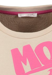 Camiseta beige de cuello redondo con letras rosas, etiqueta de marca "Key Largo XS" cosida en el interior del cuello.