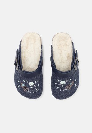 Zuecos de fieltro azul marino con forro de piel sintética blanca, con un diseño gráfico de un cohete y un planeta. Diseñados con una correa azul ajustable con hebilla.