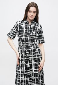 Rochie cămașă în carouri alb-negru, cu nasturi în față, mâneci scurte, talie strânsă și fustă fluidă. Material neted cu un ușor luciu.