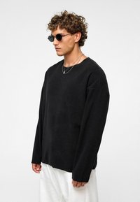 Zwarte lange mouwen shirt in een relaxte pasvorm, gemaakt van zachte stof. Heeft een brede halslijn en verlaagde schouders. G gedragen met witte pants.