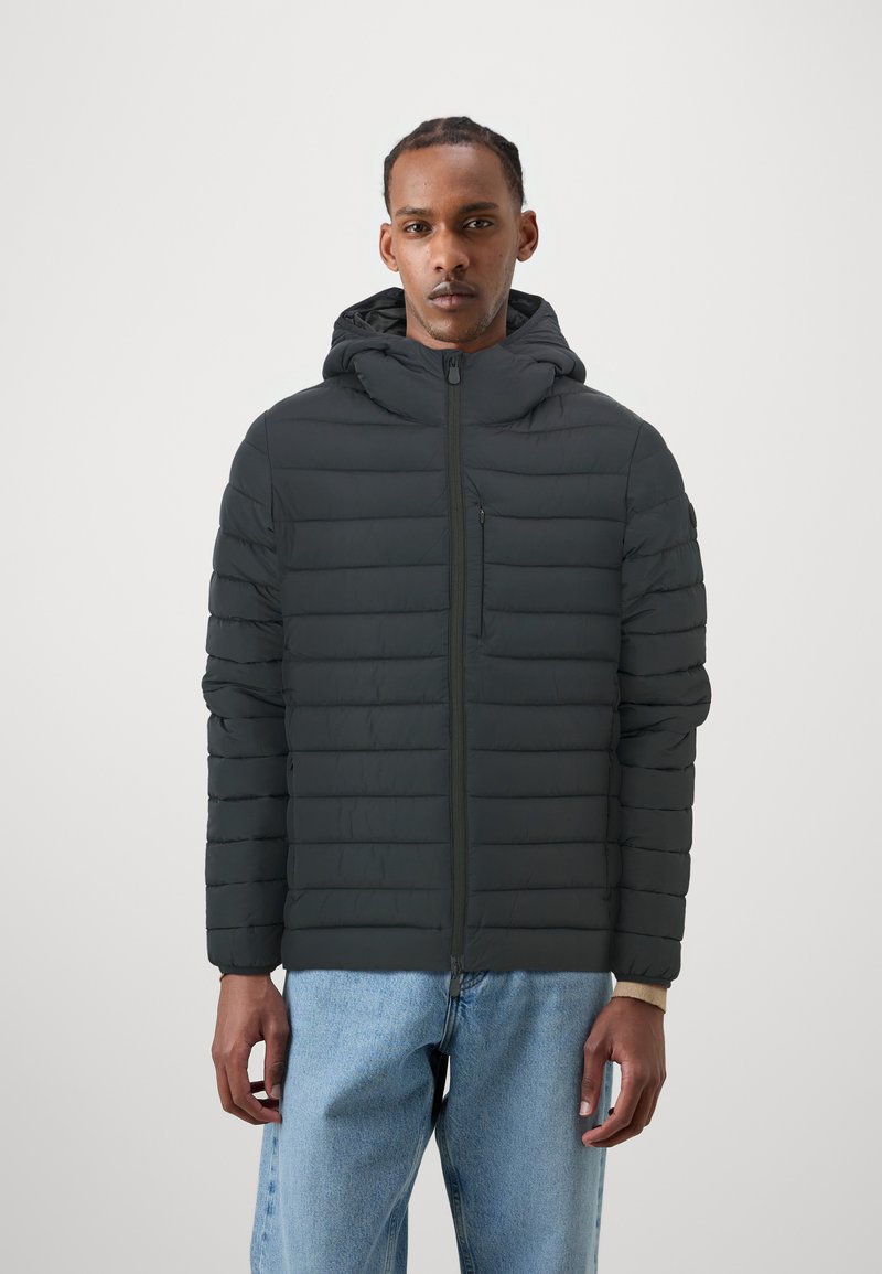 Sort puffer-jakke med horisontal quiltet mønster, fastgjort hætte, fuld frontlynlås og en lynlåslomme på brystet. Bæres med lyseblå jeans.