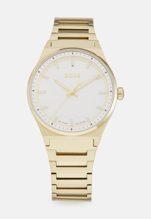 Reloj de pulsera de metal dorado con un dial blanco, marcadores de hora luminosos, manecillas delgadas y una robusta pulsera de eslabones. Resistente al agua hasta 50 metros.
