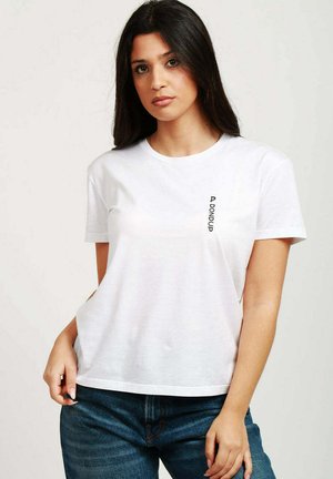 T-shirt bianco in cotone con scollo rotondo, maniche corte e un piccolo logo nero stampato verticalmente sul lato sinistro.