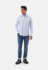 Hellblaues Hemd mit Kragen, getragen mit blauen Jeans und schwarzen Schnürschuhen. Das Hemd hat eine glatte Textur und lange Ärmel.