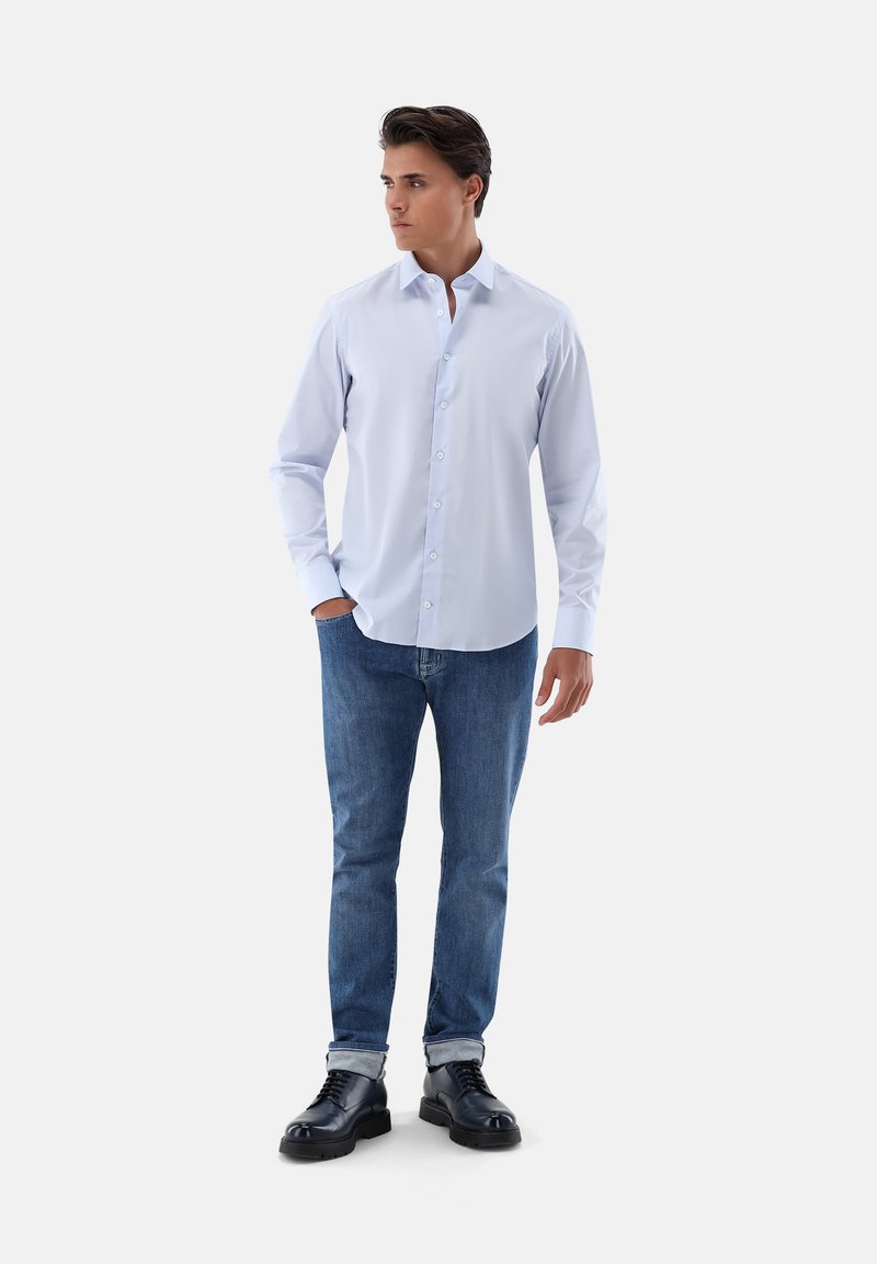 Hellblaues Hemd mit Kragen, getragen mit blauen Jeans und schwarzen Schnürschuhen. Das Hemd hat eine glatte Textur und lange Ärmel.