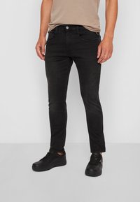 Svarta denimjeans med smal passform, som har en klassisk design med fem fickor, subtil blekning och stängning med knapp och dragkedja. Bärs med svarta skor.