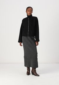 Black zip-up jacket with a high collar, paired with a fitted, ribbed gray maxi skirt and brown heeled boots.