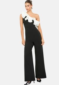 Zwarte jumpsuit met een wijde pijp-silhouette, voorzien van een enkele witte rucheschouder. Gemaakt van een gladde stof, zonder zichtbare patronen of accenten.