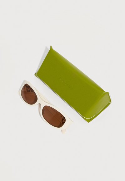 Lunettes de soleil à monture blanche avec des verres bruns à côté d'un étui rectangulaire fermé de couleur vert olive sur un fond blanc.