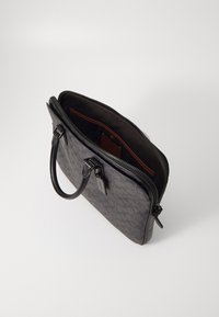 Black patterned leather handbag with dual handles and a zip closure. Interior features a brown lining and a small pocket with a tag.