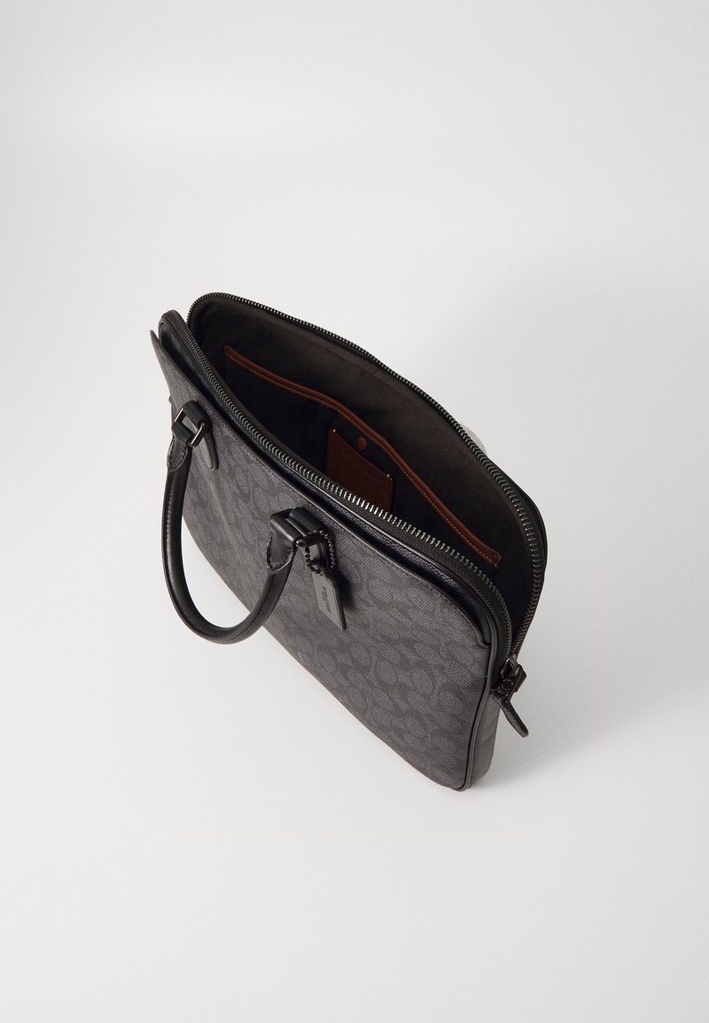 Borsa a tracolla in pelle nera con motivo, dotata di due manici e chiusura con zip. L'interno presenta una fodera marrone e una tasca piccola con etichetta.