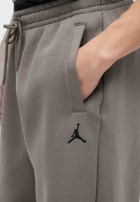Graue Jogginghosen mit elastischem Bund, Kordelzug, Seitentaschen und einem schwarzen Jordan-Logo am linken Oberschenkel, gefertigt aus weichem Material.