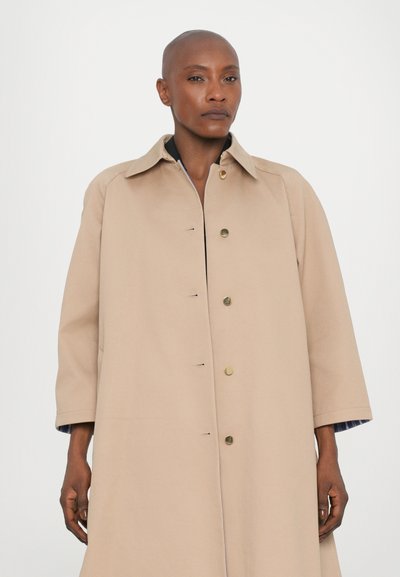 Cappotto oversize beige con colletto a punta, chiusura frontale a pressione e due tasche laterali. Presenta una texture liscia e una vestibilità comoda.