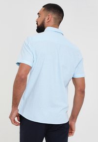 Camicia azzurro chiaro a maniche corte realizzata in un tessuto morbido e testurizzato. Presenta un colletto button-down e un orlo dritto con spacchi laterali.