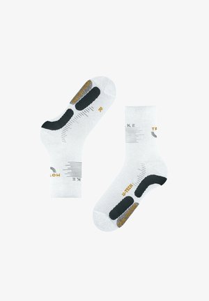 White ankle socks with black and gold accents. Features textured grip patterns on the bottom and printed labels indicating fit and technology.