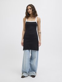 Vestido preto com textura e alças brancas, combinado com jeans de perna larga em azul claro. Detalhes notáveis incluem um decote quadrado e um tecido texturizado.