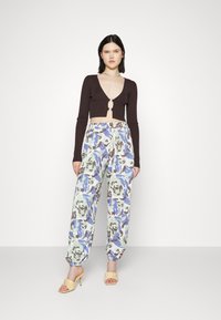 Top crop canelado castanho com um decote em V profundo e um detalhe de fecho metálico, combinado com calças largas com padrão floral em tons de verde menta, azul e castanho.