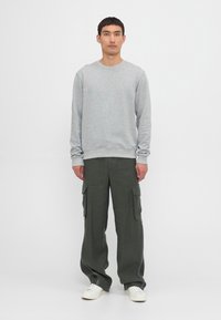 Gray crewneck sweatshirt in soft fabric, paired with olive green cargo pants featuring multiple pockets. Footwear is white sneakers.