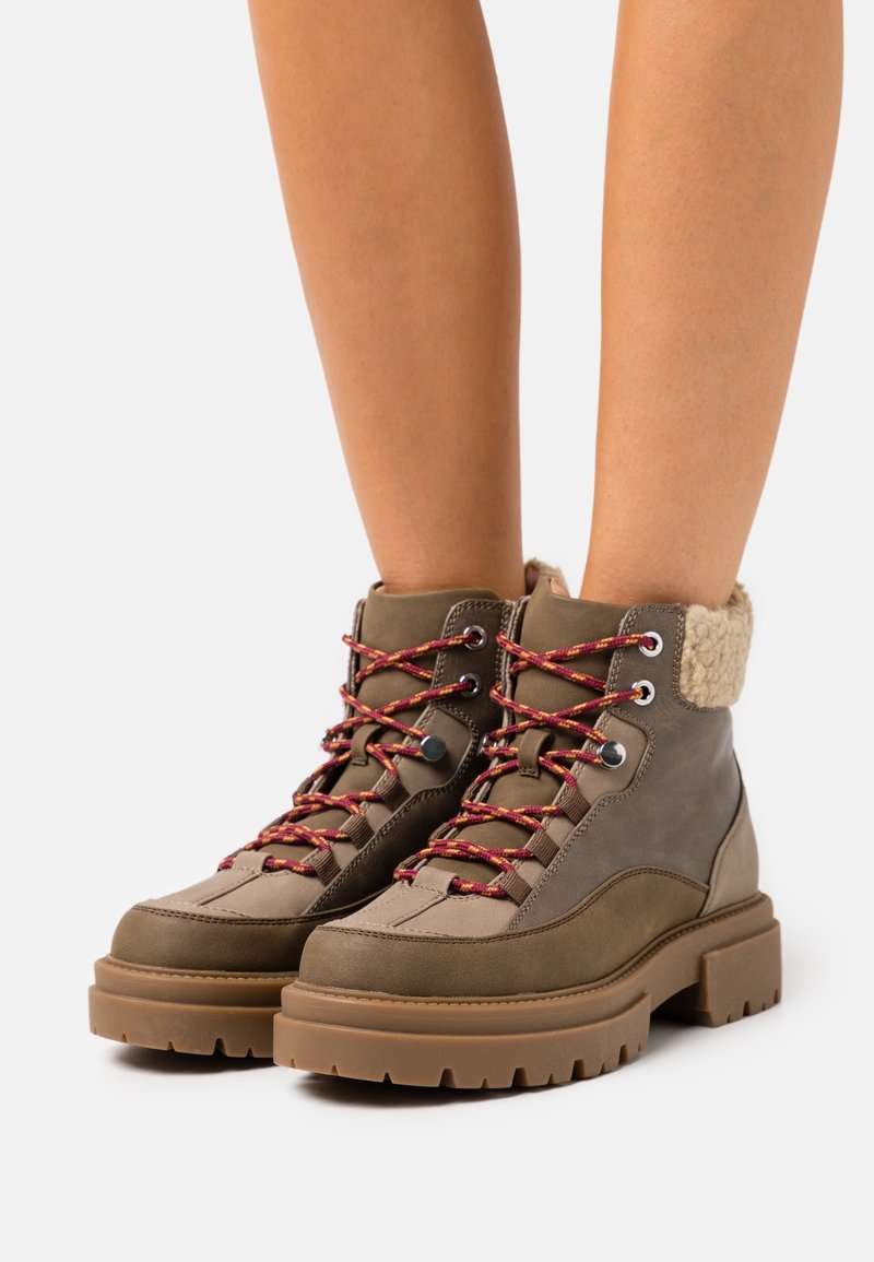 Stivali da trekking marroni con suola spessa, realizzati in materiale testurizzato, con lacci rossi e gialli a contrasto e un colletto morbido di colore crema.