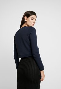 Pulôver azul-marinho cortado com mangas longas, decote redondo e textura suave, combinado com uma saia preta canelada. Design simples e minimalista.