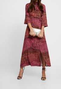 Sukienka maxi z wzorem gradientowym w odcieniach różu i pomarańczu, z rękawami dzwonowymi, przednim rozcięciem oraz dopasowaną metaliczną kopertówką.