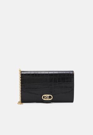 Musta krokotiilin nahkainen clutch-laukku kultaisella ketjuhihnalla ja kultaisella ovaalilla lukolla, jossa on toisiinsa limittyvät alkukirjaimet.