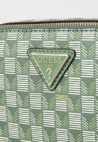 Borsa a mano verde con motivo a zigzag, dotata di un logo in metallo dorato a forma triangolare e tessuto testurizzato che presenta disegni a spina di pesce e righe alternate.