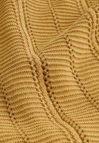 Gros plan sur un tissu tricoté jaune moutarde doux et texturé avec un motif côtelé et des lignes diagonales en relief créant une apparence chaleureuse et confortable.