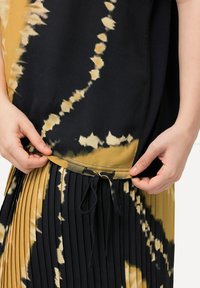 Šaty v černé a žluté barvě s tie-dye vzorem a sklady. Mají stahovací šňůrku v pase a hladkou texturu látky.