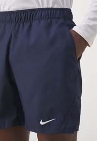 Nike maudymosi šortai tamsiai mėlynos spalvos, elastingas audinys, elastinga juosta, šoninės kišenės, papuošti balta logotipu kairiajame šlaunyje.