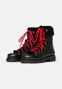 Botas de invierno de cuero negro con forro de piel sintética negra y gruesos cordones rojos brillantes, ubicadas una al lado de la otra sobre un fondo blanco.