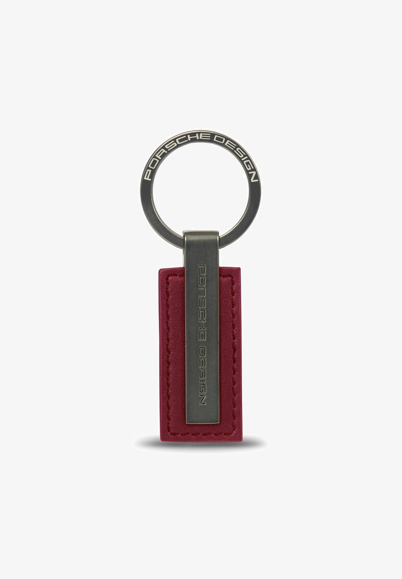 Llave de Porsche Design con una etiqueta de cuero burdeos y herrajes metálicos plateados, con grabado de la marca y un robusto anillo de sujeción.