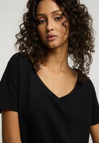 Czarny t-shirt z dekoltem w serek, wykonany z miękkiego materiału, z krótkimi rękawami i luźnym krojem, podkreślający gładką fakturę.