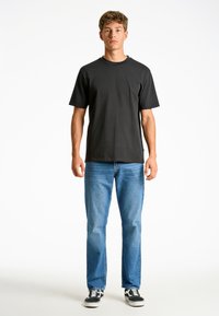 T-shirt nera a maniche corte con collo rotondo, abbinata a jeans a gamba dritta azzurri e sneaker nere. Stile semplice e casual.