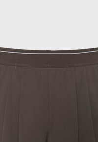 Pantalon gris foncé avec une large ceinture élastique comportant une fine bande blanche horizontale, tissu lisse avec des coutures verticales subtiles.