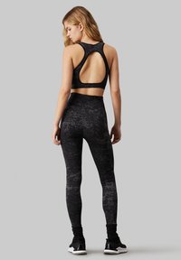 Completo sportivo nero composto da un top corto con schiena scoperta e leggings a vita alta, entrambi con un motivo testurizzato e marmorizzato.