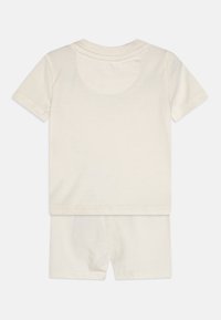 Conjunto de camiseta de manga corta y pantalones cortos de color crema, hecho de suave algodón. Presenta un cuello redondo y un simple dobladillo cosido.