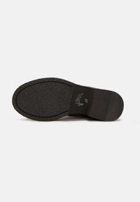 Semelle de chaussure noire avec surface en caoutchouc texturée. Présente un bord lisse et un nom de marque embossé. Design à talon pour l'élévation.