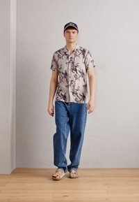 Short-sleeve shirt with a multicolored abstract pattern, paired with loose-fitting blue jeans and beige sandals. Simple design and casual style.