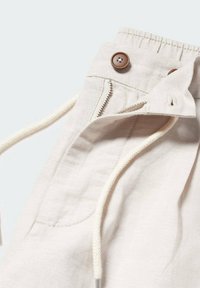 Pantalon en lin beige avec cordon de serrage et fermeture éclair, doté d'un bouton marron et d'une poche latérale. Tissu texturé avec une finition douce.